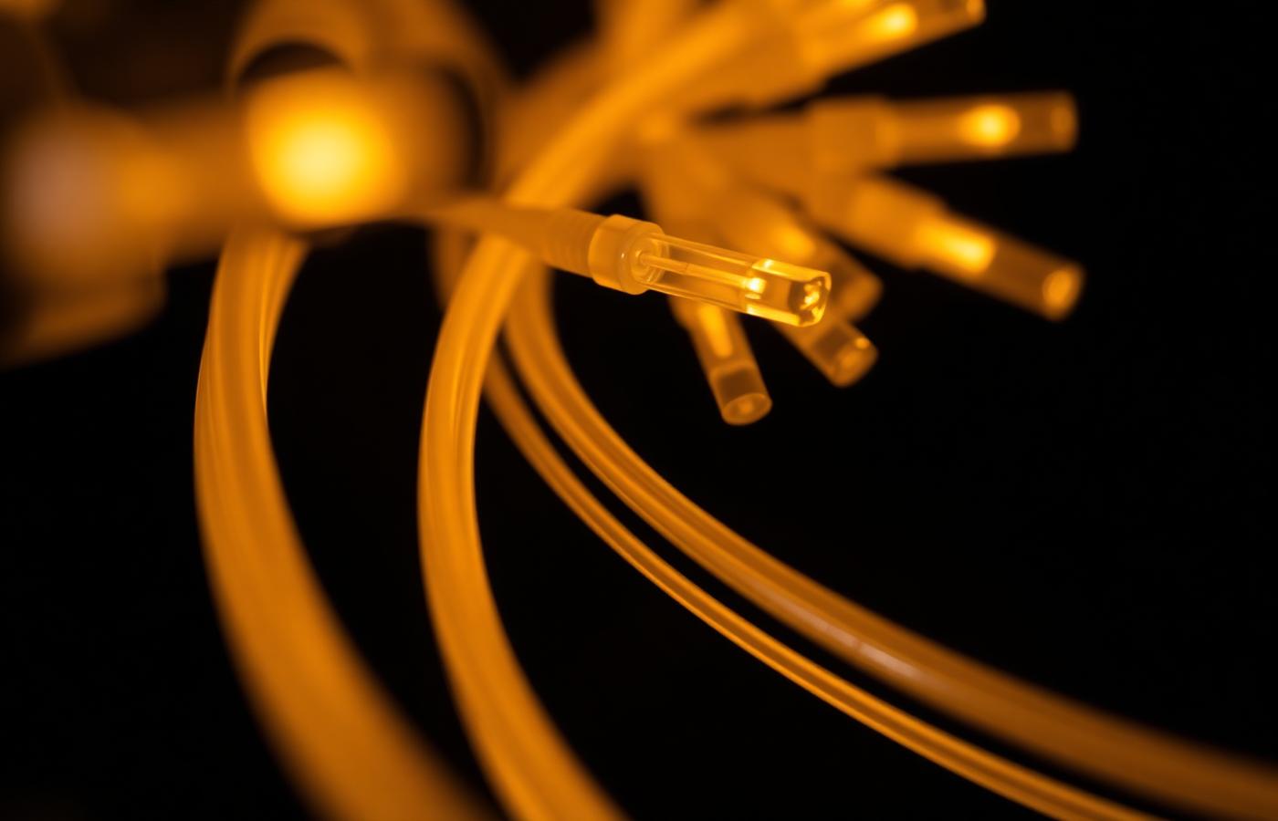 Bundle of illuminated fibre optic cables glowing amber against a dark background